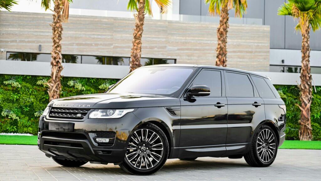 Black Range Rover SUV parked on a paved driveway with palm trees and modern building in the background