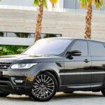 Black Range Rover SUV parked on a paved driveway with palm trees and modern building in the background