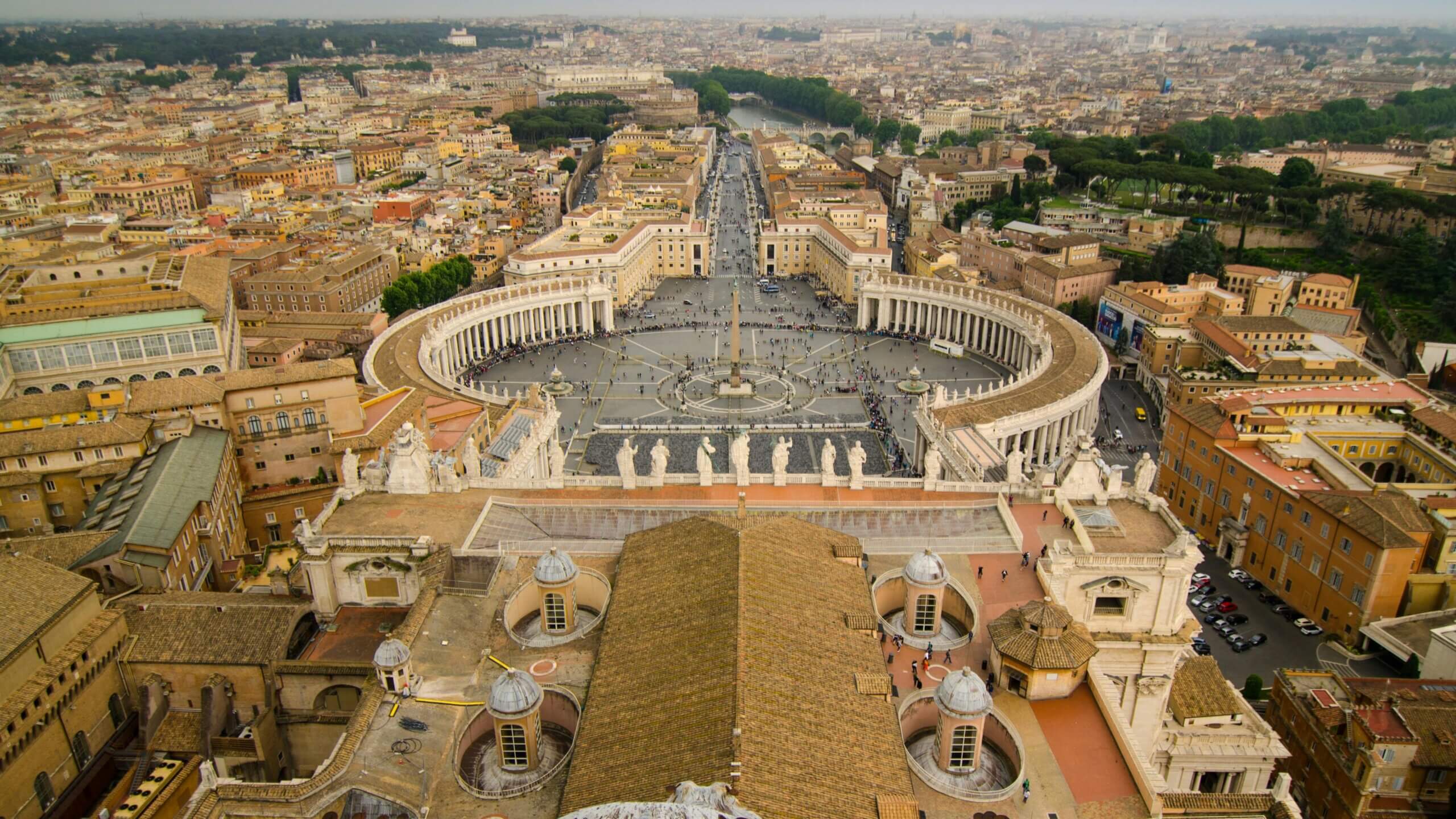 Aerial view of St. Peter's Square and surrounding buildings in Vatican City with people walking around the plaza.