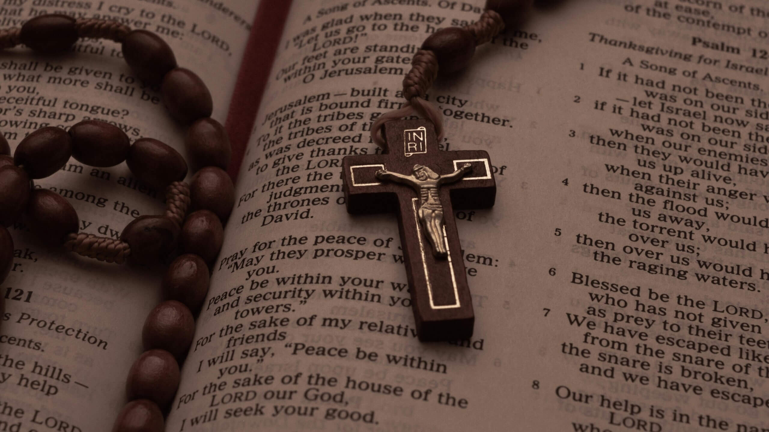 Wooden rosary with crucifix resting on an open Bible showing Psalm 121 and Psalm 123 text.