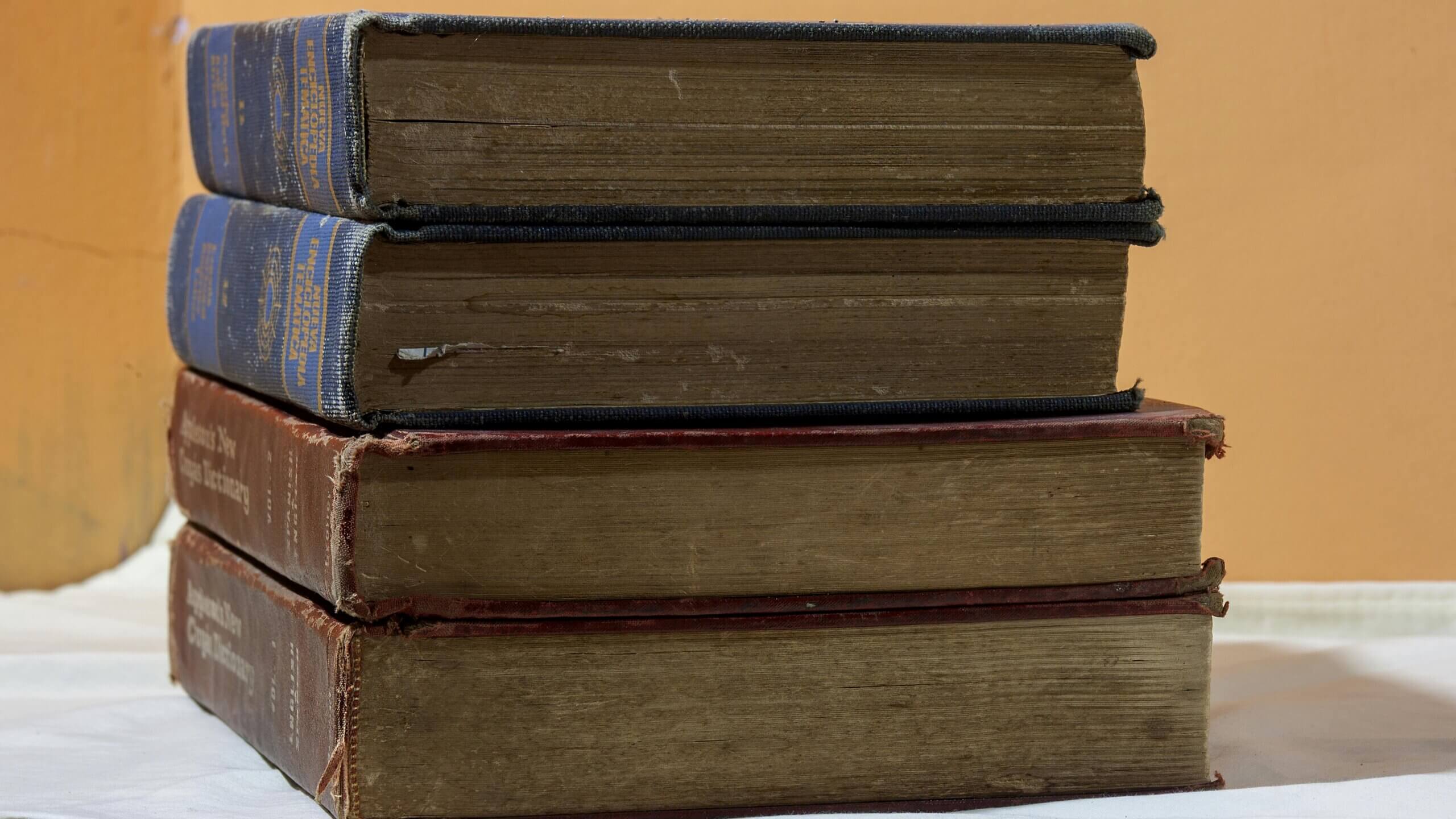 Stack of four old hardcover books with worn edges, two with blue spines and two with red spines