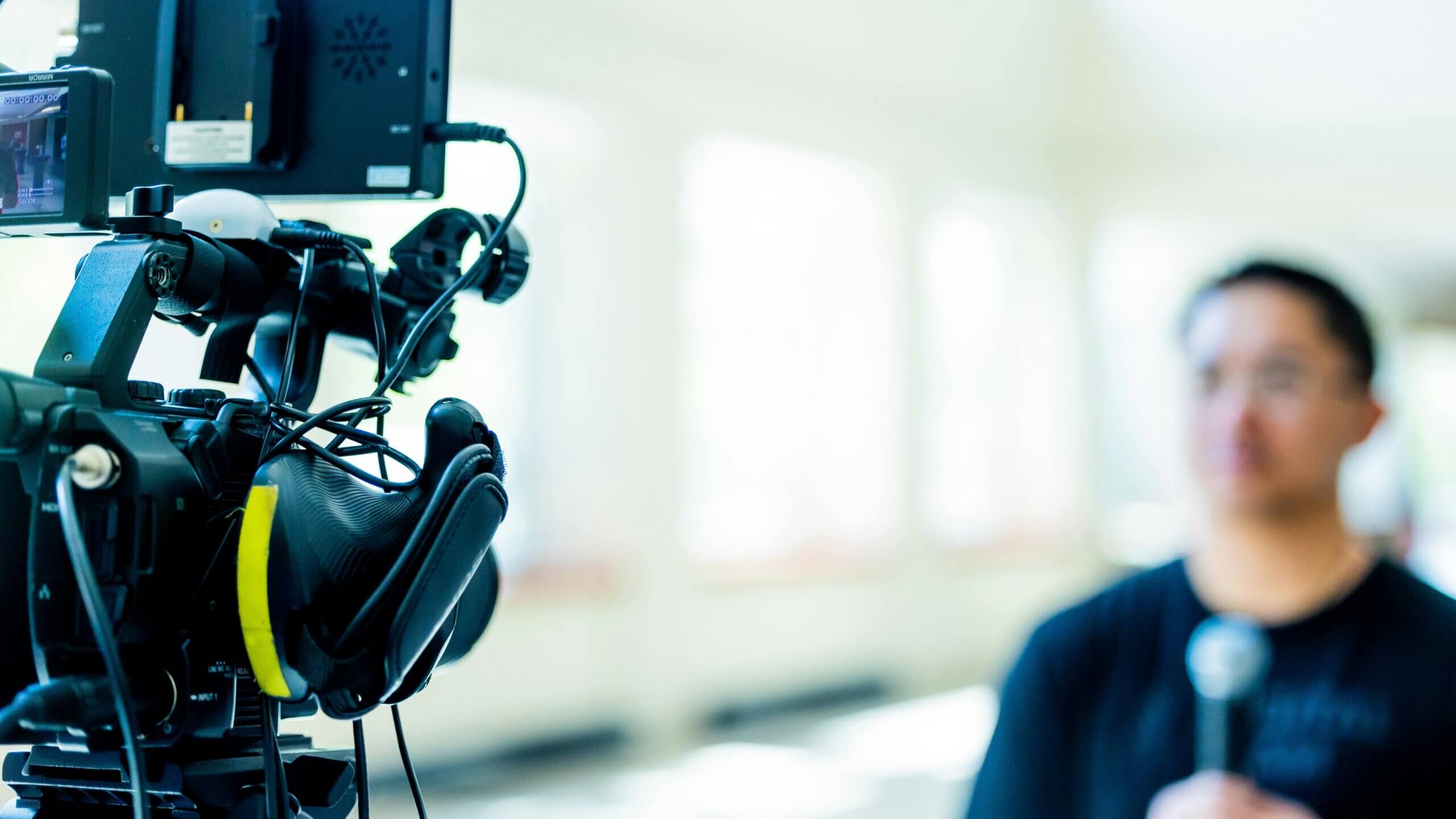 professional video camera focused on recording a person holding a microphone in a bright room