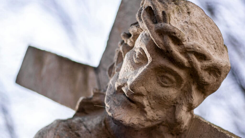 Close-up of a stone statue of Jesus wearing a crown of thorns carrying a cross.