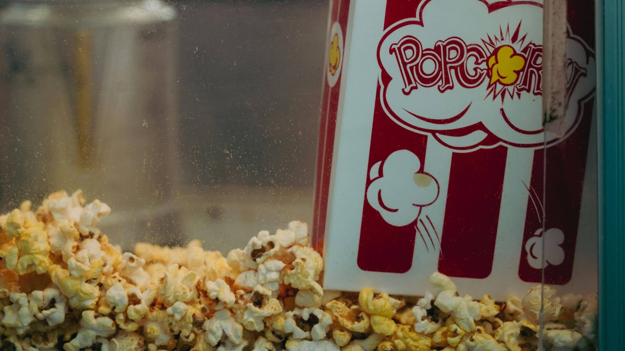 Popcorn overflowing from a red and white striped popcorn container inside a popcorn machine.