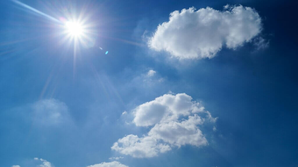 Bright sun shining in a clear blue sky with scattered white clouds