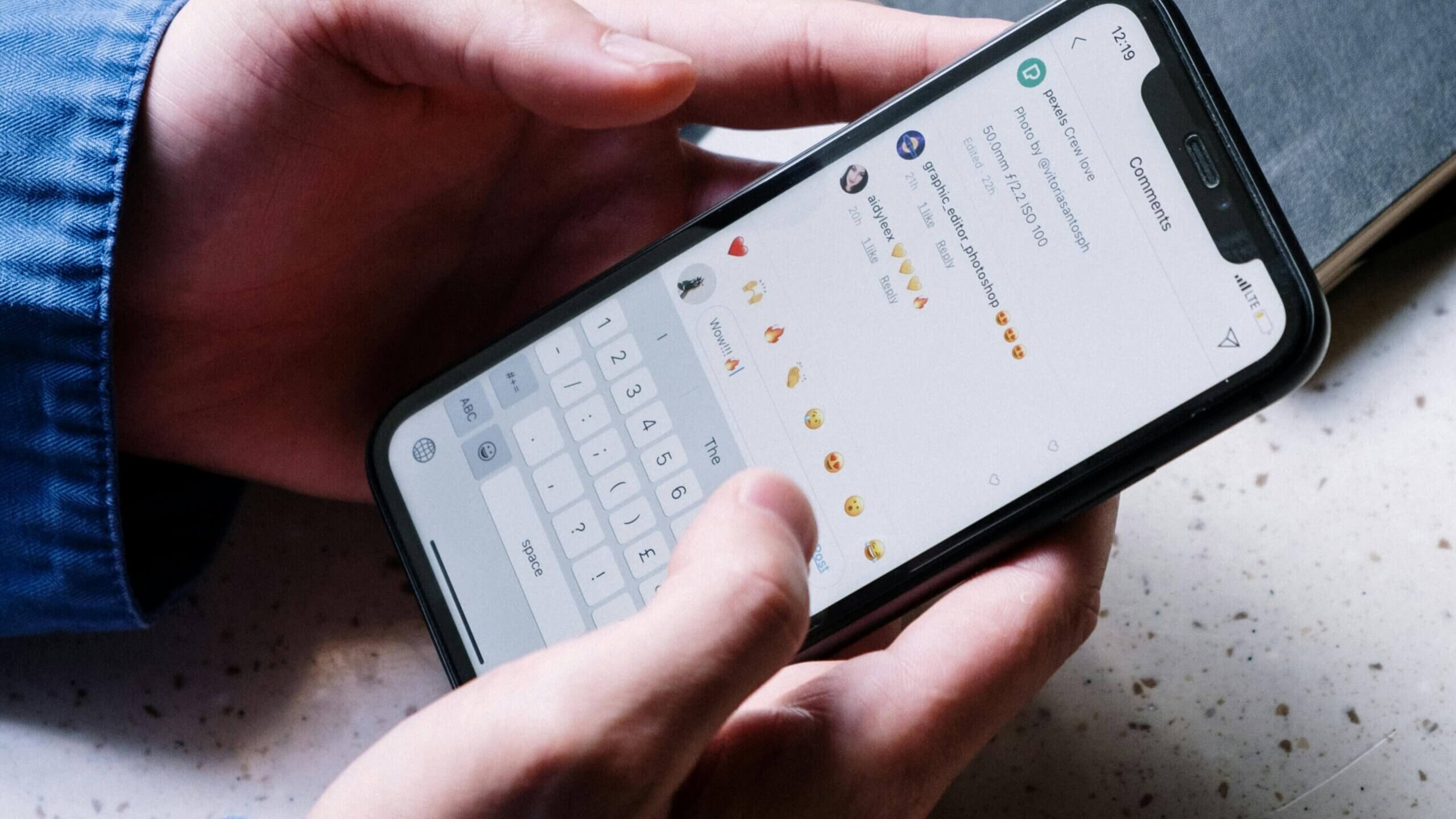 Person typing a comment with emojis on a smartphone social media app under a post by Pexels Crew Love