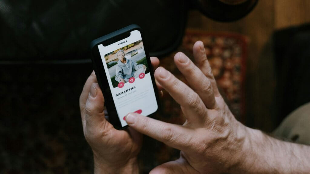 Person using a dating app on a smartphone, viewing a profile named Samantha, 55 years old, with interaction buttons visible.