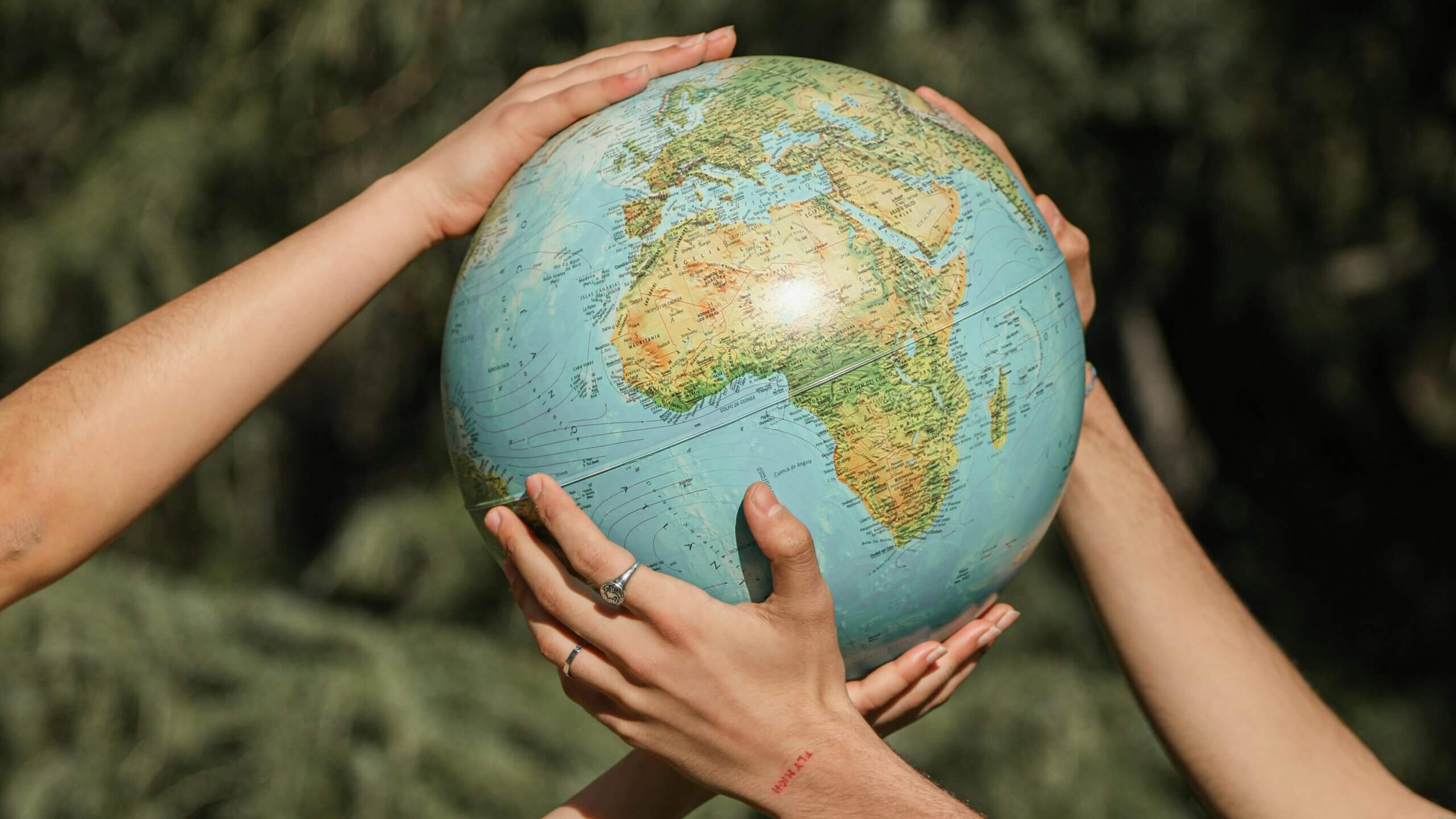 Four hands holding a globe showing Africa and surrounding continents against a blurred outdoor background