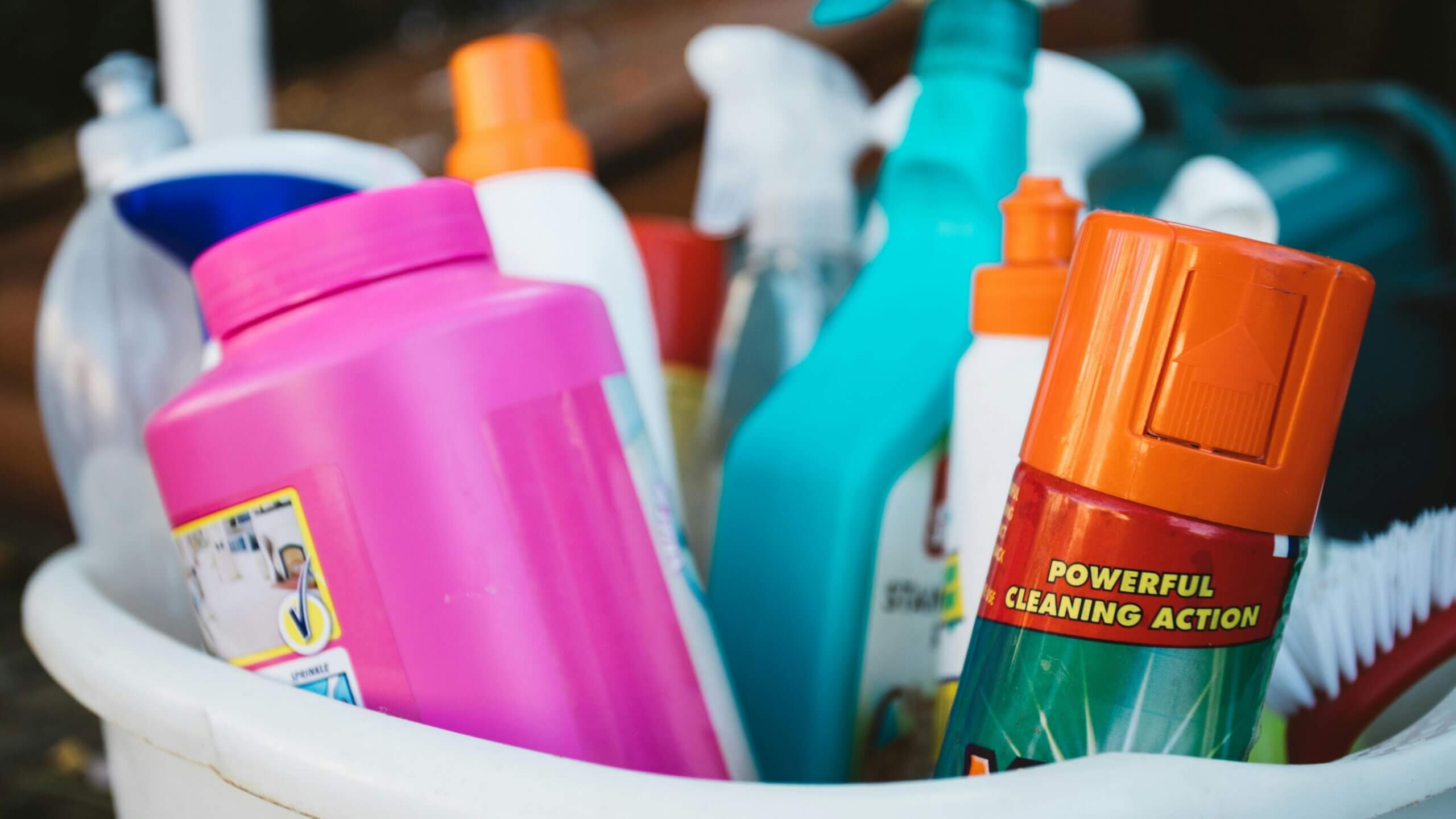 Assorted colorful cleaning product bottles and a brush in a white container
