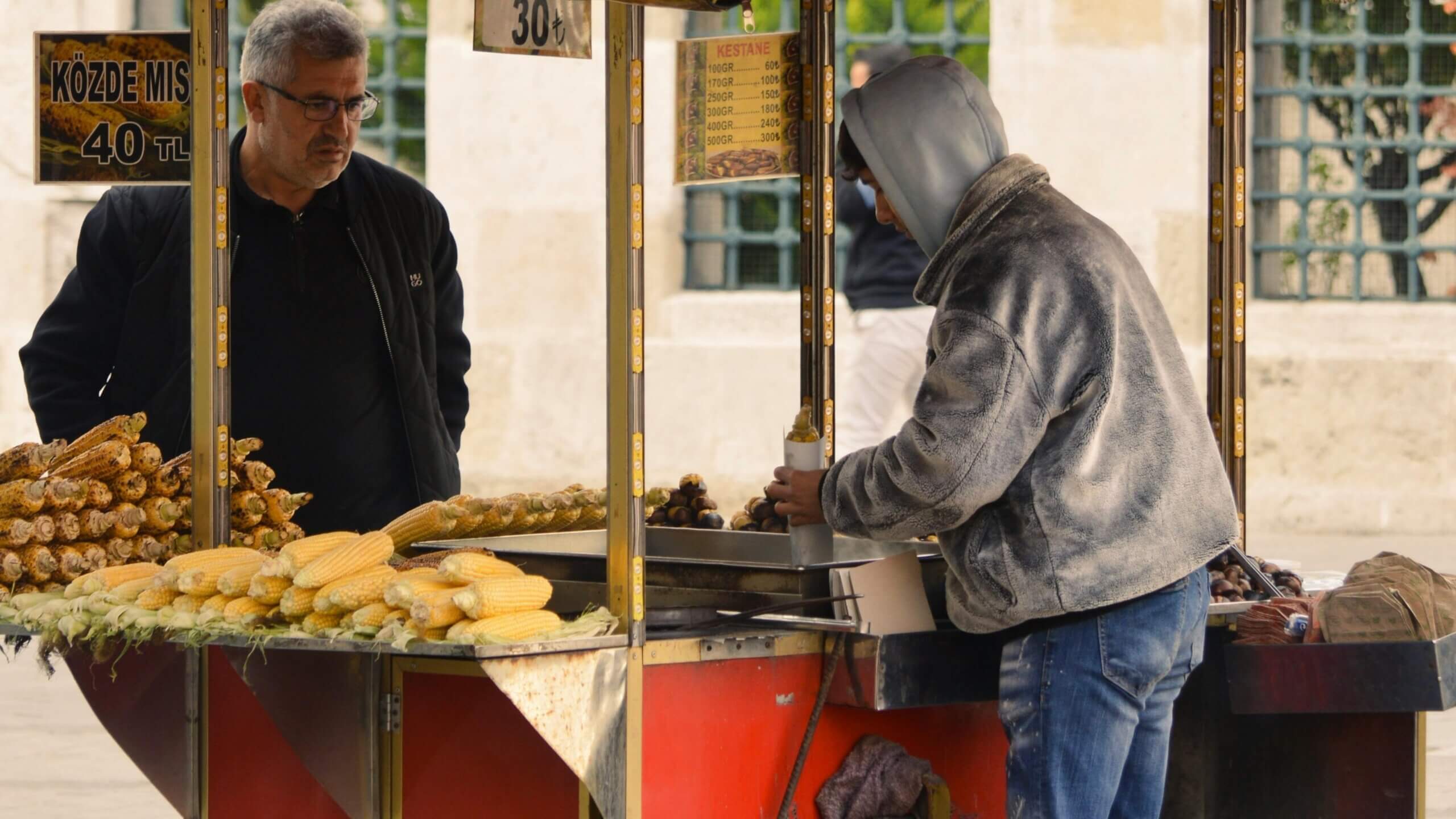 Vendor serving roasted chestnuts and corn to a customer at a street food cart in Turkey.