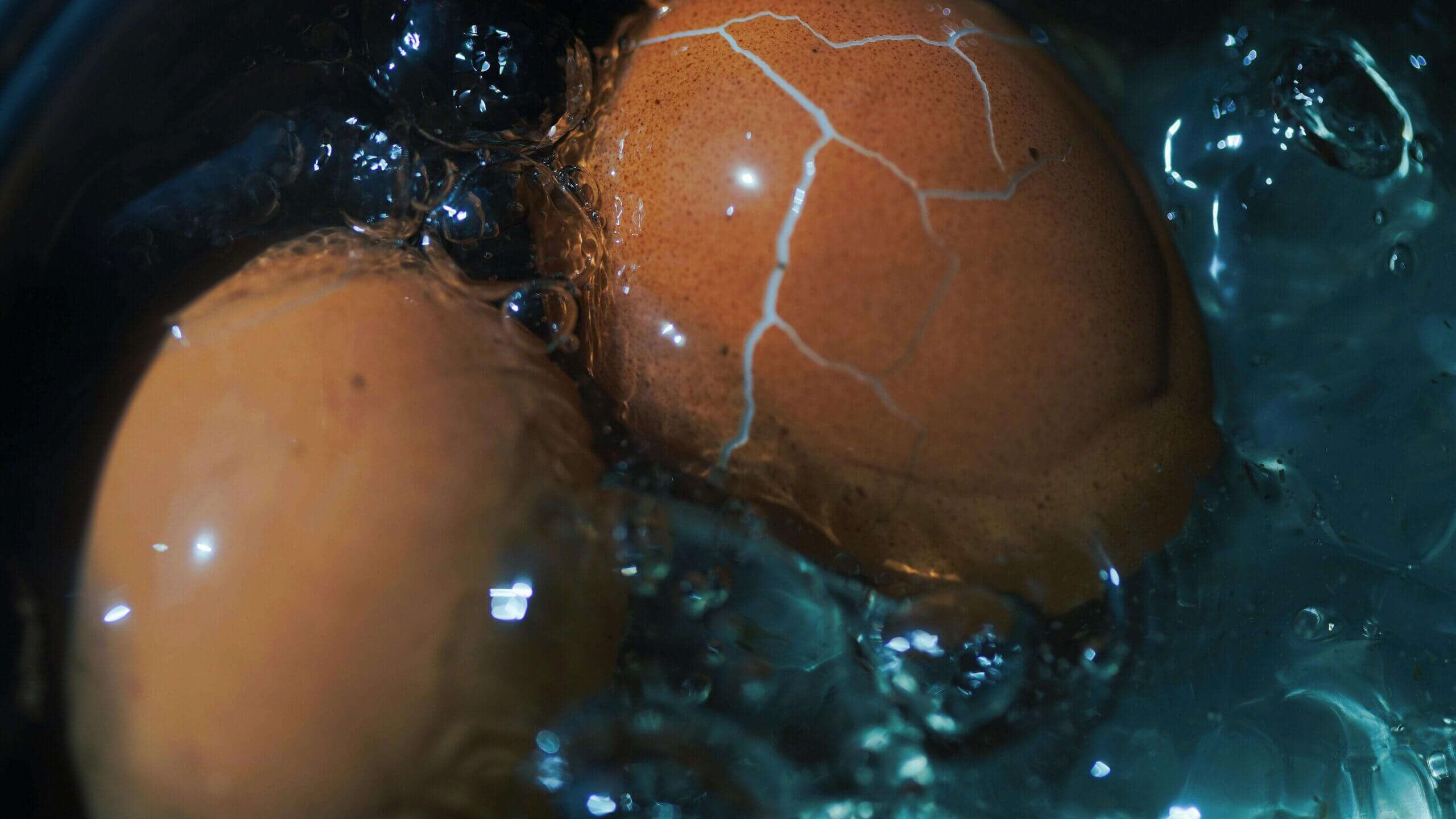Two brown eggs, one cracked, boiling in bubbling water