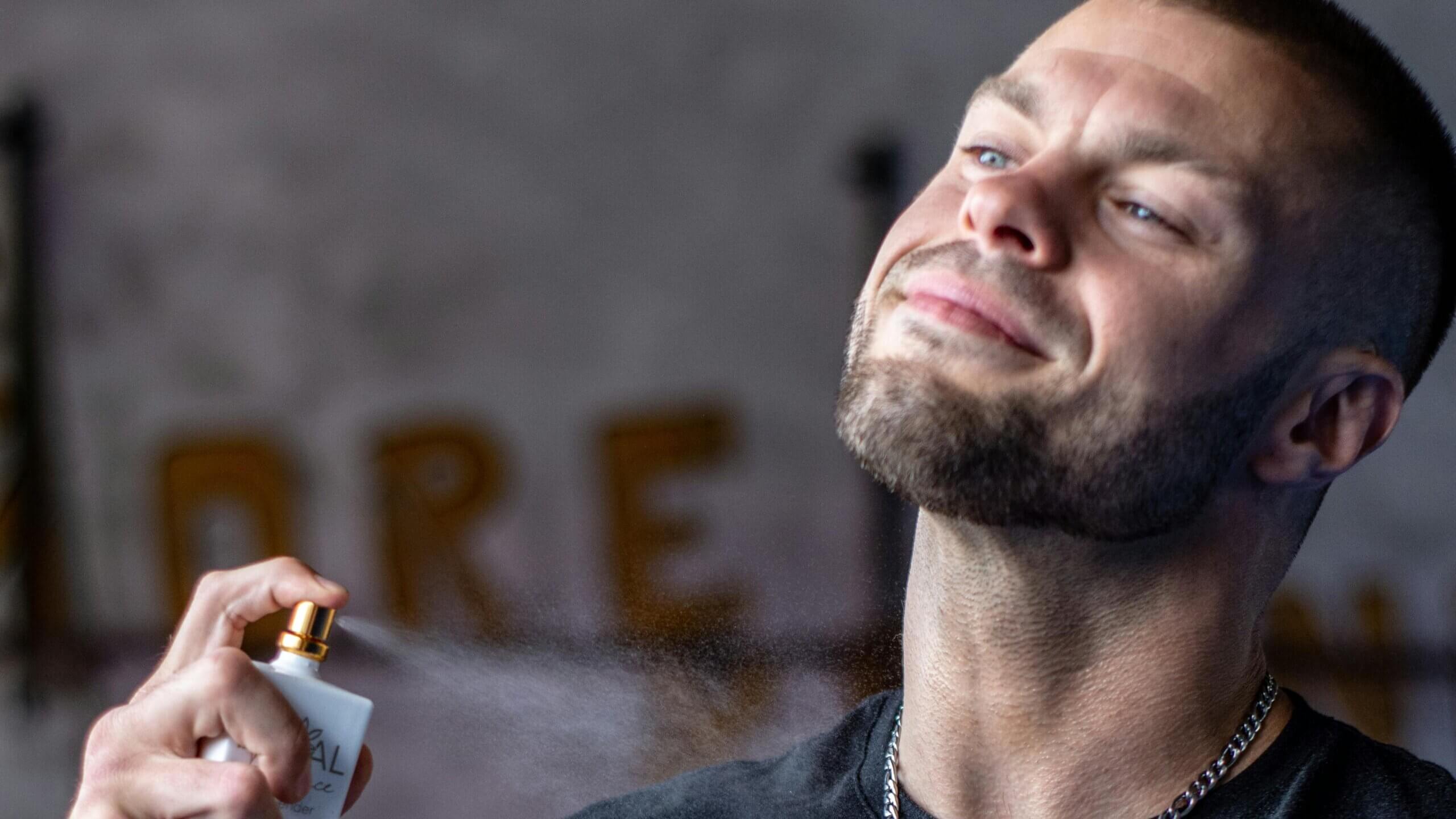 Man spraying L'Oréal Paris fragrance on his neck with a slight smile