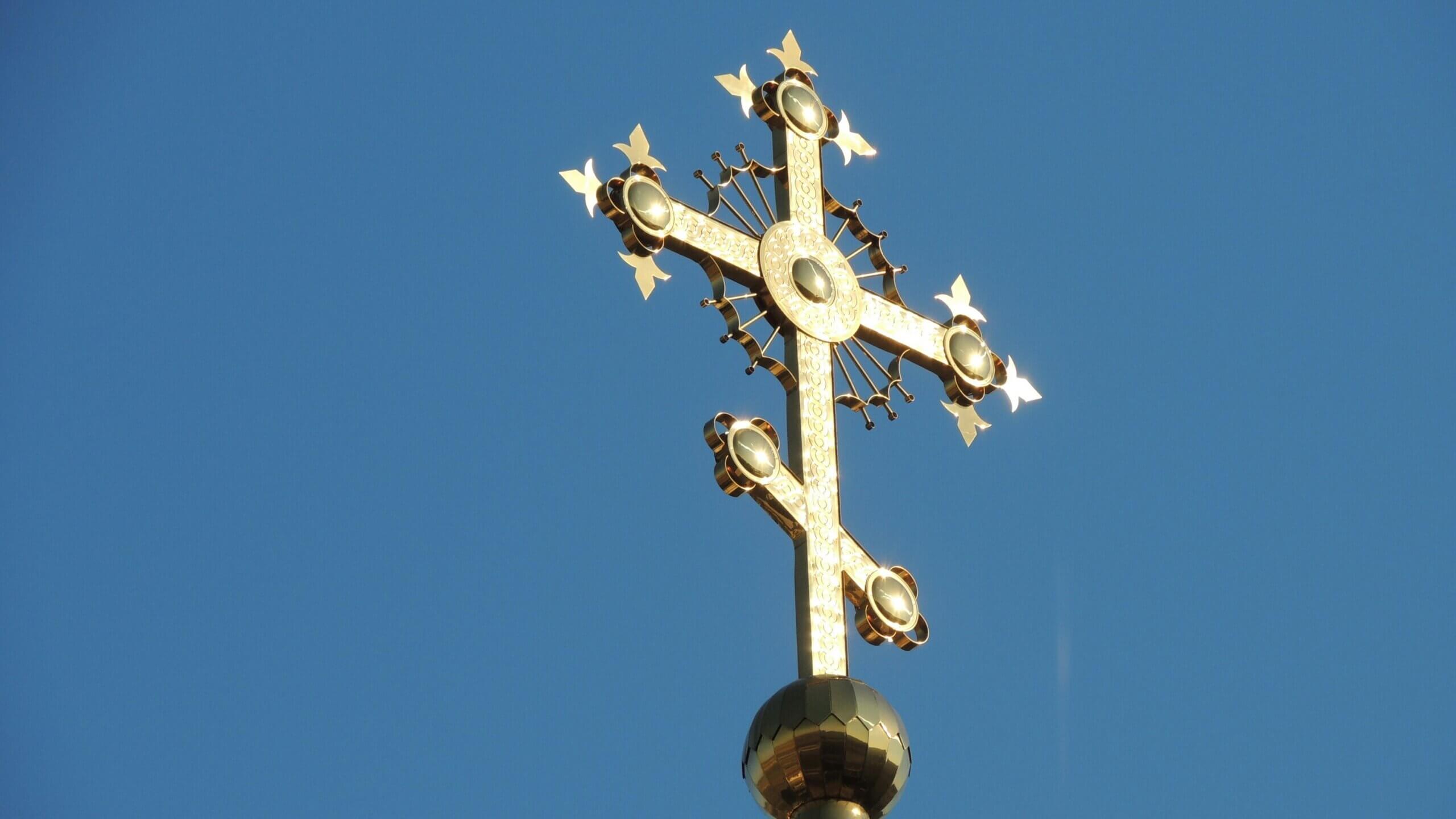 Golden ornate cross atop a dome against a clear blue sky