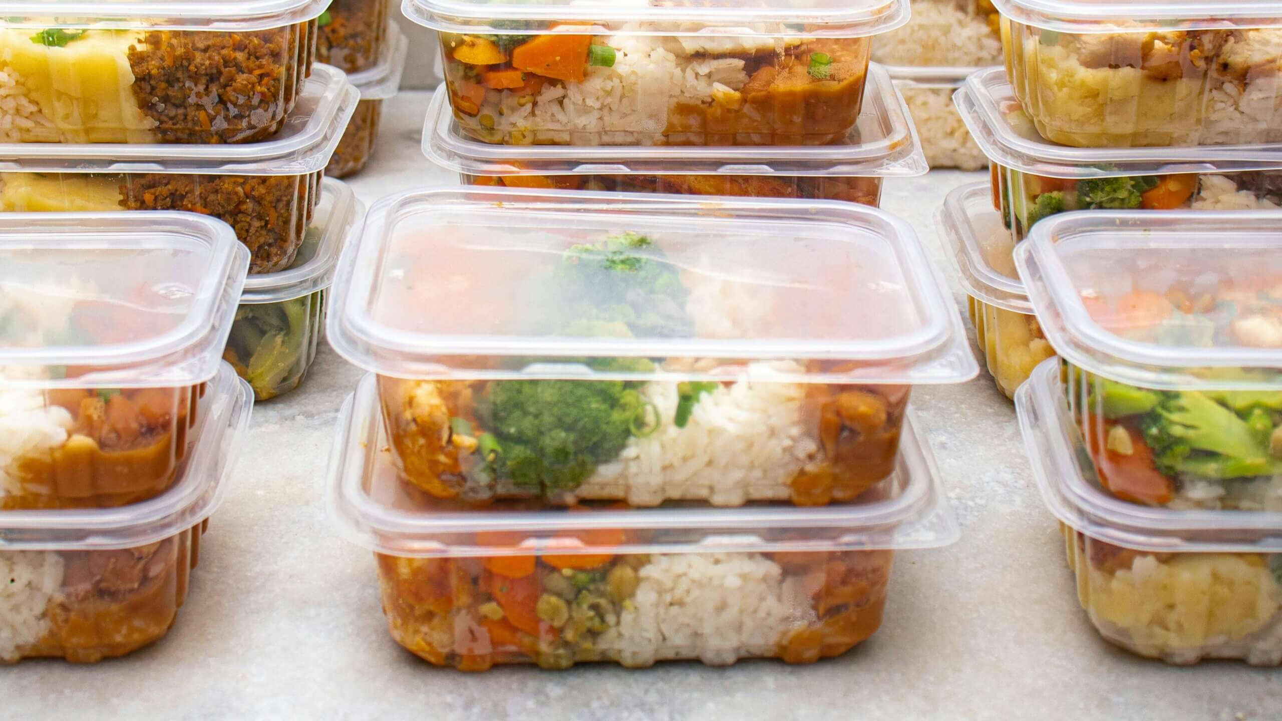 Stacked plastic containers filled with rice, vegetables, and curry meal prep portions.
