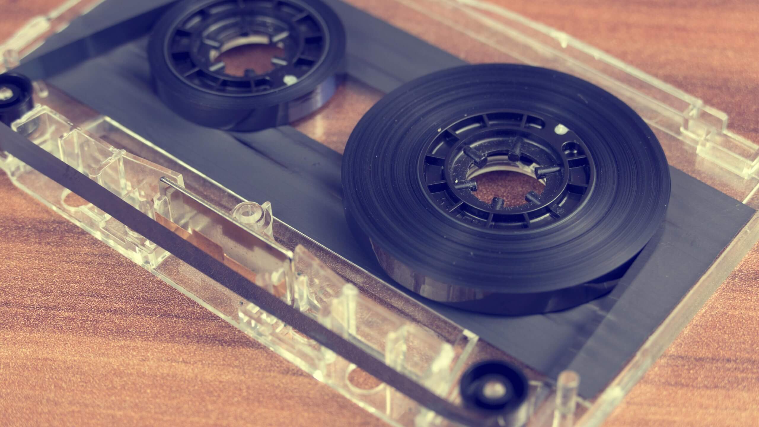 Close-up of a transparent cassette tape with black magnetic tape reels on a wooden surface