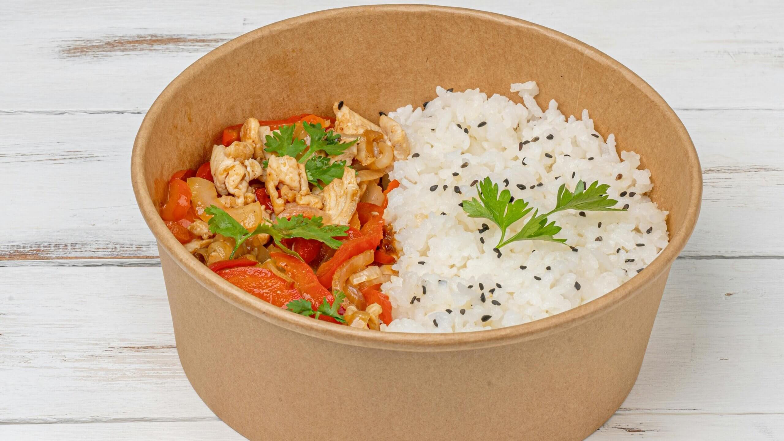 Takeout bowl with white rice garnished with black sesame seeds and cooked chicken with vegetables and parsley leaves