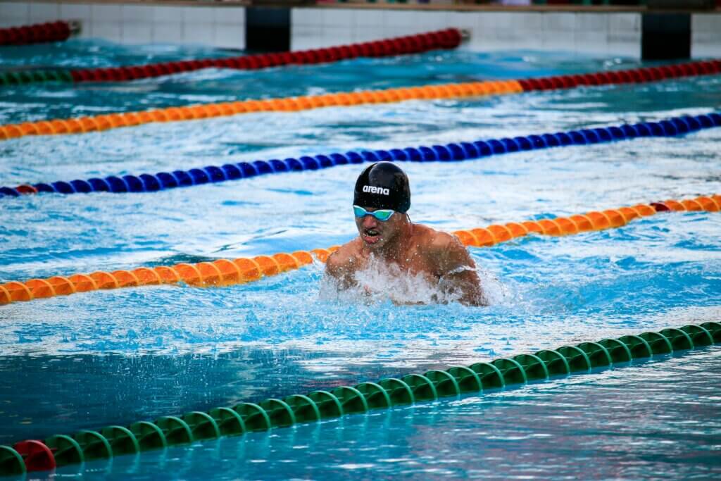 Swimmer wearing Arena cap and goggles performing breaststroke in a pool with lane dividers