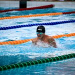 Swimmer wearing Arena cap and goggles performing breaststroke in a pool with lane dividers