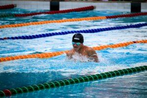 Swimmer wearing Arena cap and goggles performing breaststroke in a pool with lane dividers