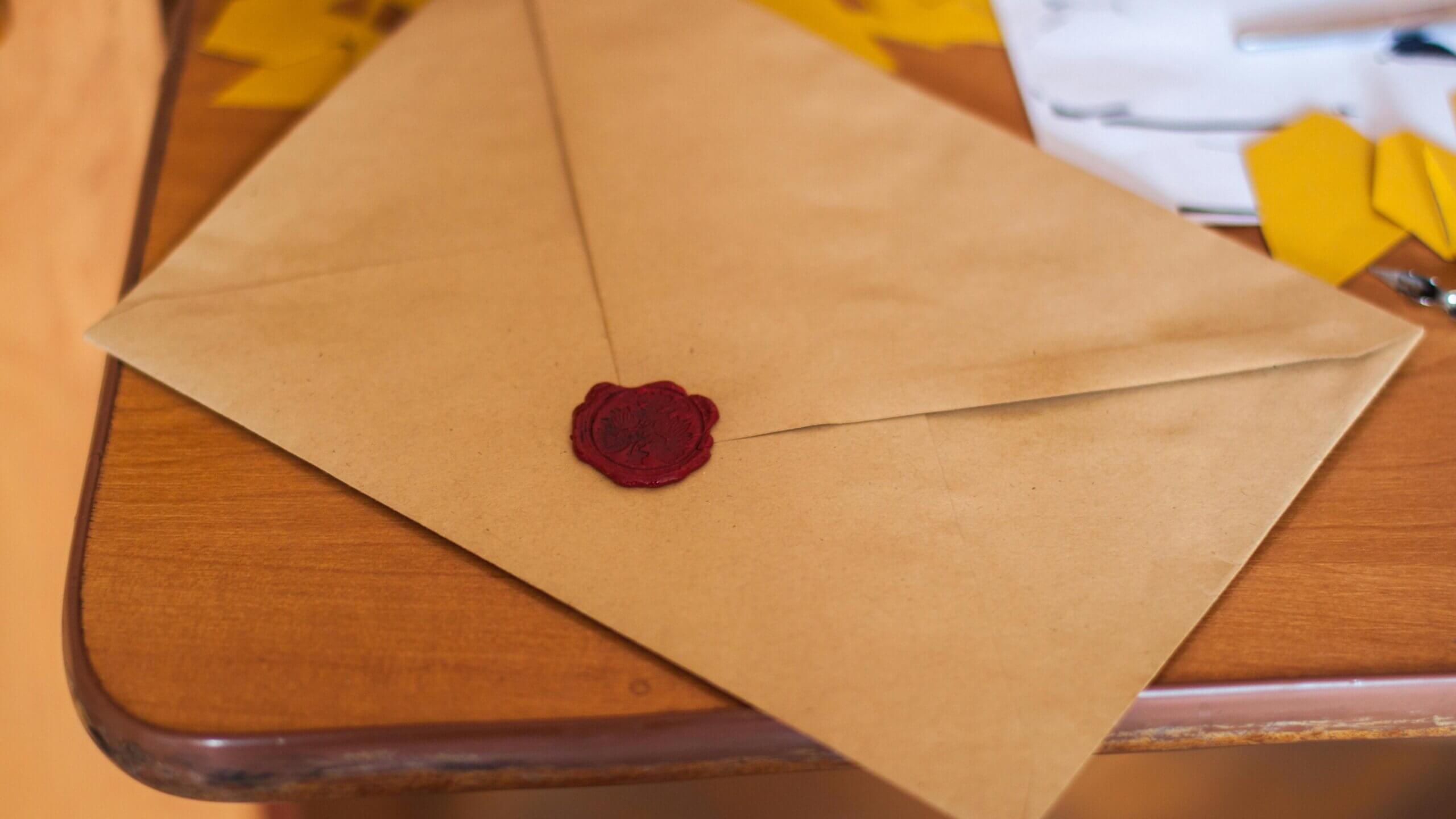 Brown envelope sealed with a red wax seal on a wooden table with papers and yellow shapes nearby