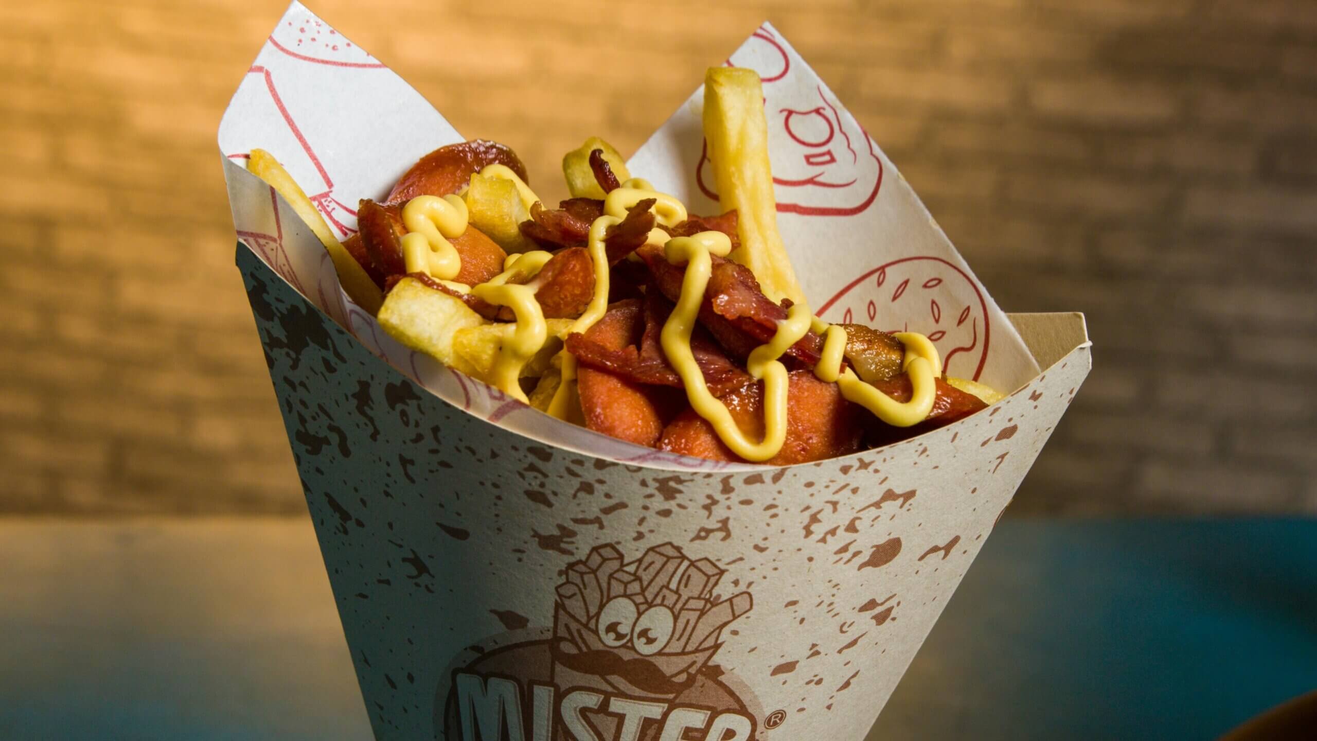 Mister fries cone with bacon, sausage slices, and mustard drizzle on top
