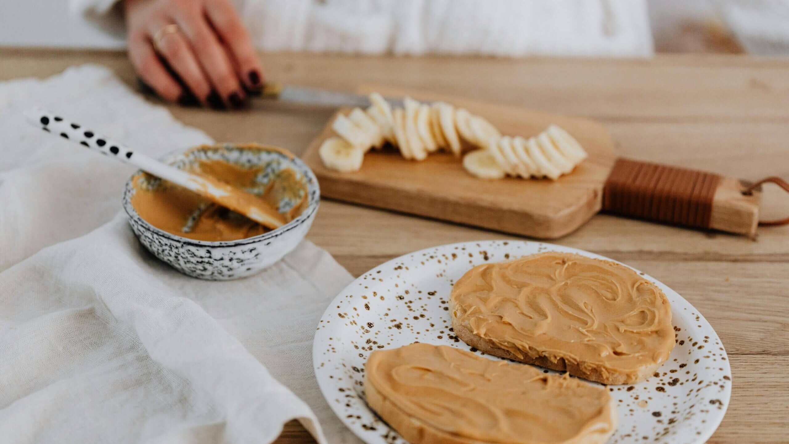 Slices of banana on a cutting board with peanut butter spread on two slices of bread on a speckled plate
