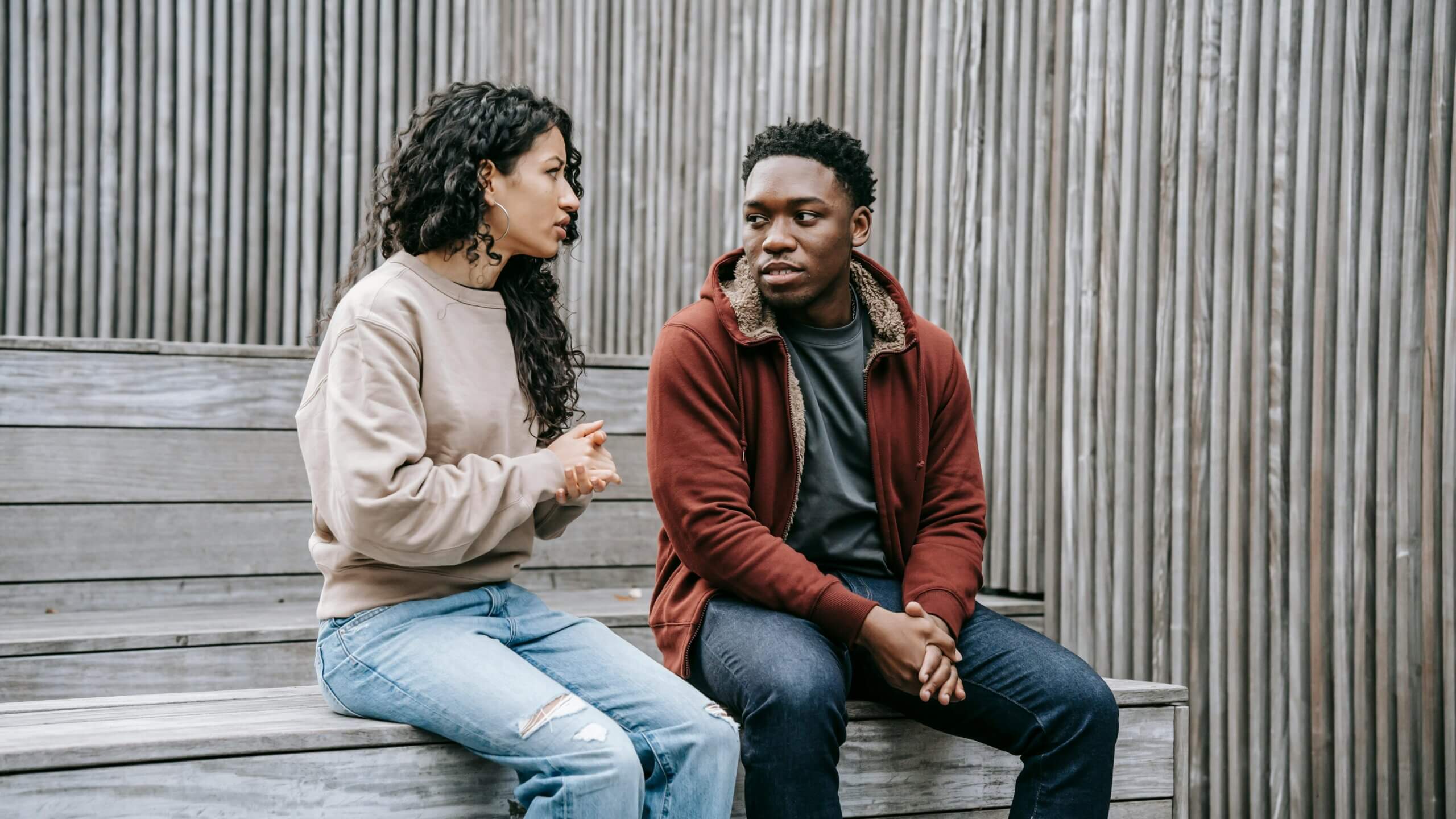 Two young adults sitting on wooden benches having a serious conversation outdoors.
