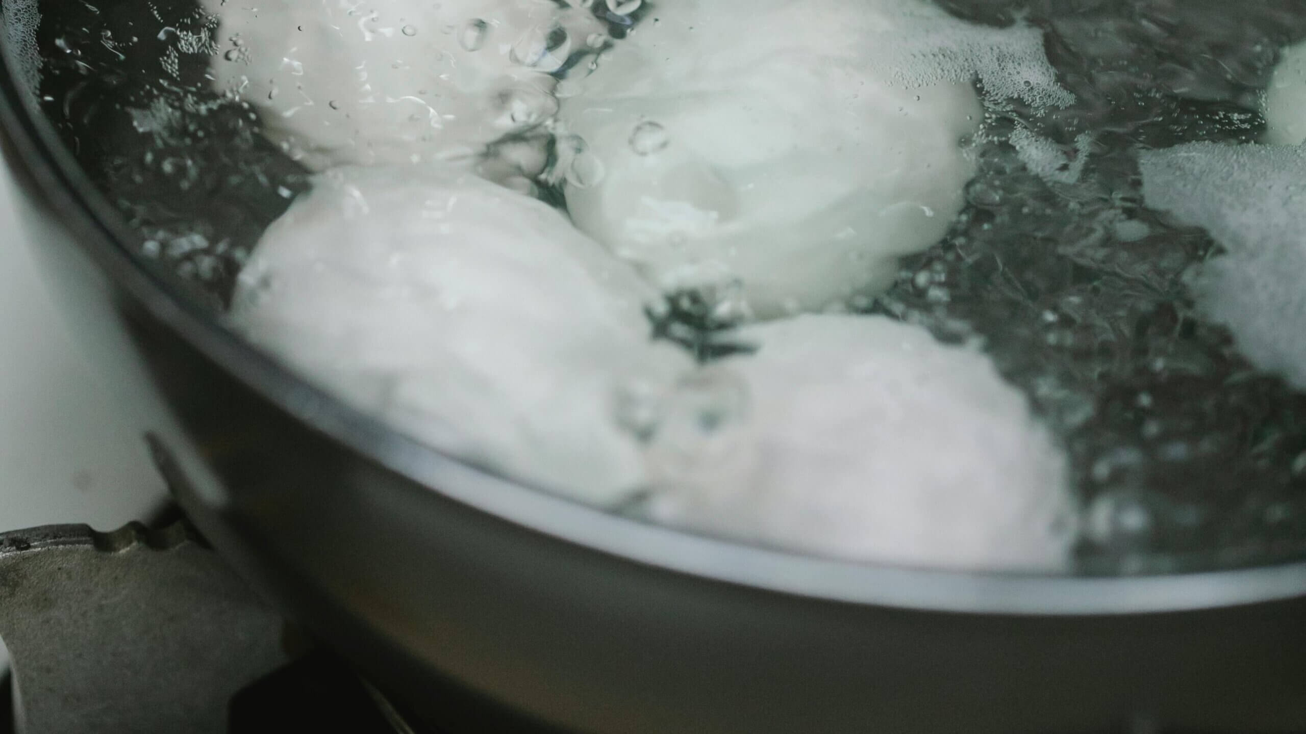 Four white eggs boiling in a pot of bubbling water on a stove burner