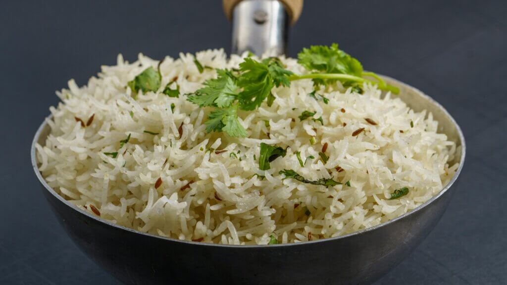 Steamed basmati rice garnished with cumin seeds and fresh cilantro in a metal serving spoon