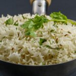 Steamed basmati rice garnished with cumin seeds and fresh cilantro in a metal serving spoon