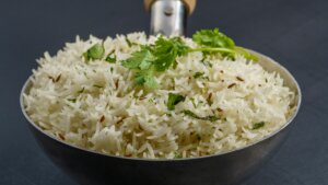 Steamed basmati rice garnished with cumin seeds and fresh cilantro in a metal serving spoon