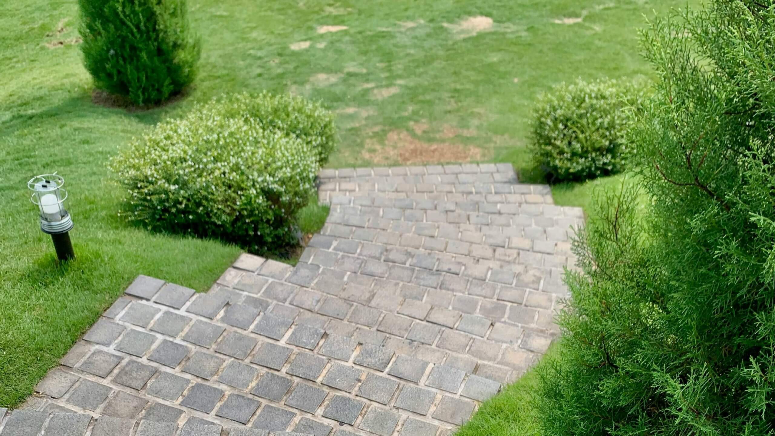 Stone steps leading down to a grassy garden area with bushes and a small outdoor lantern light.