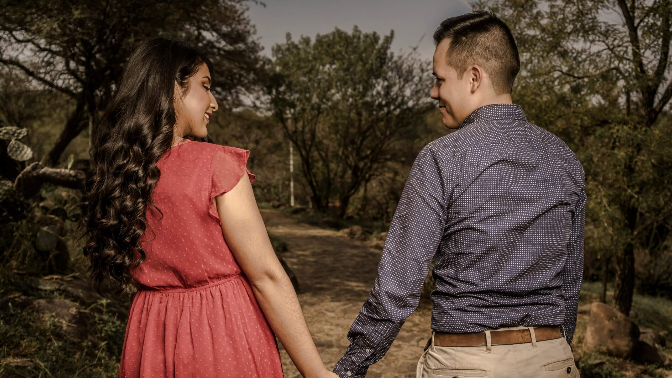 Couple holding hands and smiling at each other while walking on a forest path