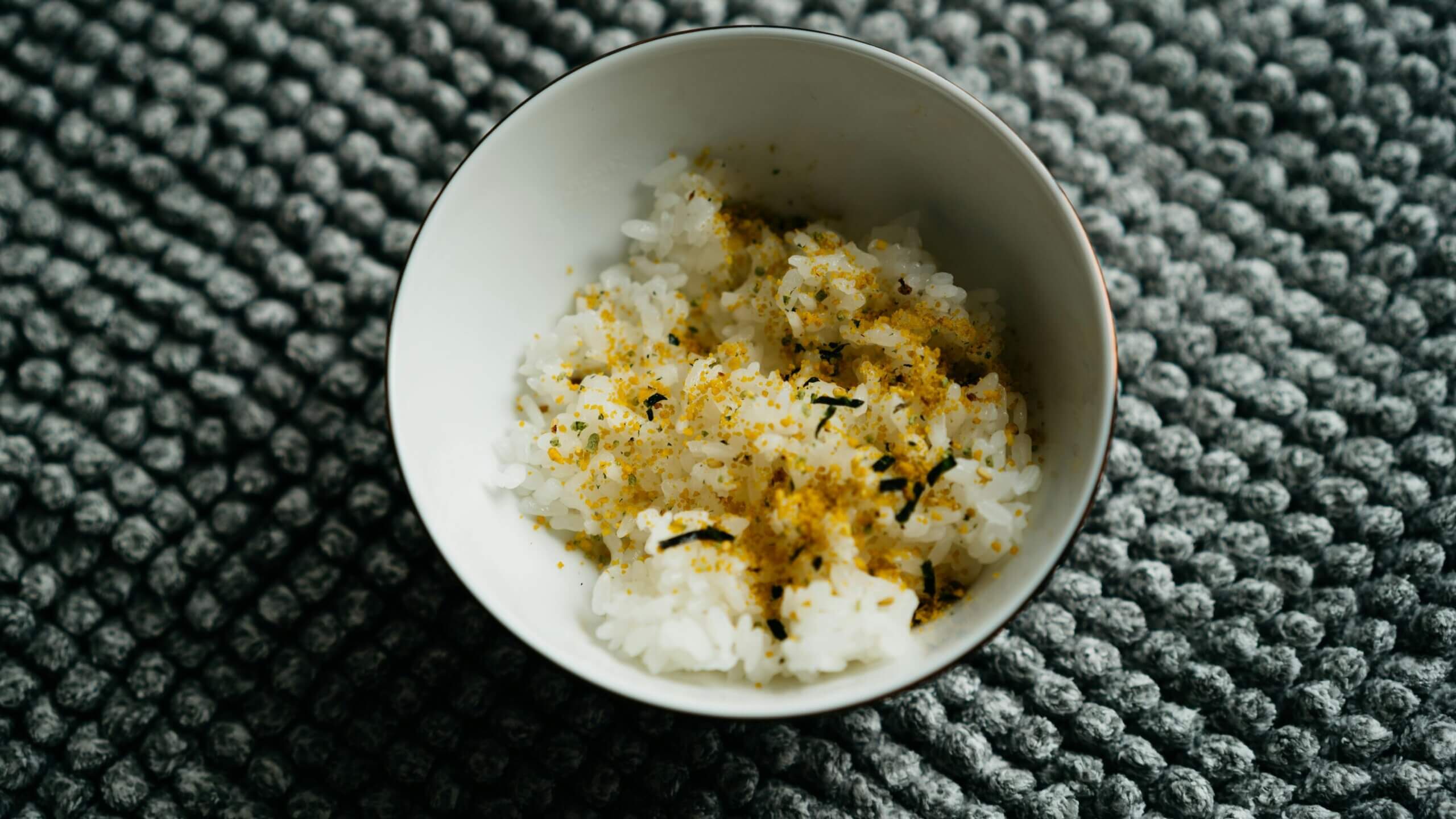 Bowl of white rice sprinkled with yellow seasoning on a textured gray surface