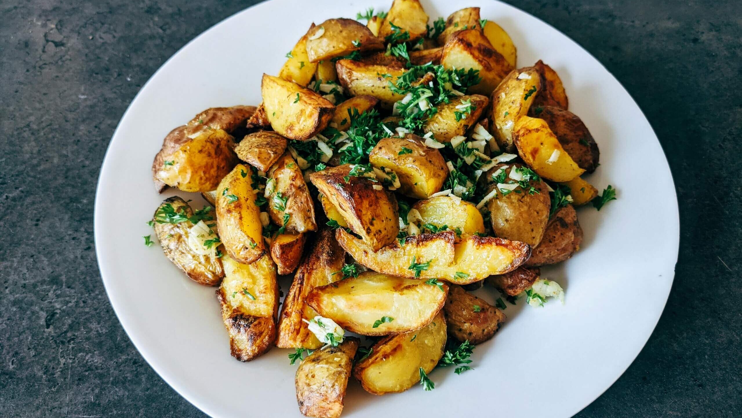 Roasted potato wedges garnished with chopped garlic and fresh parsley on a white plate