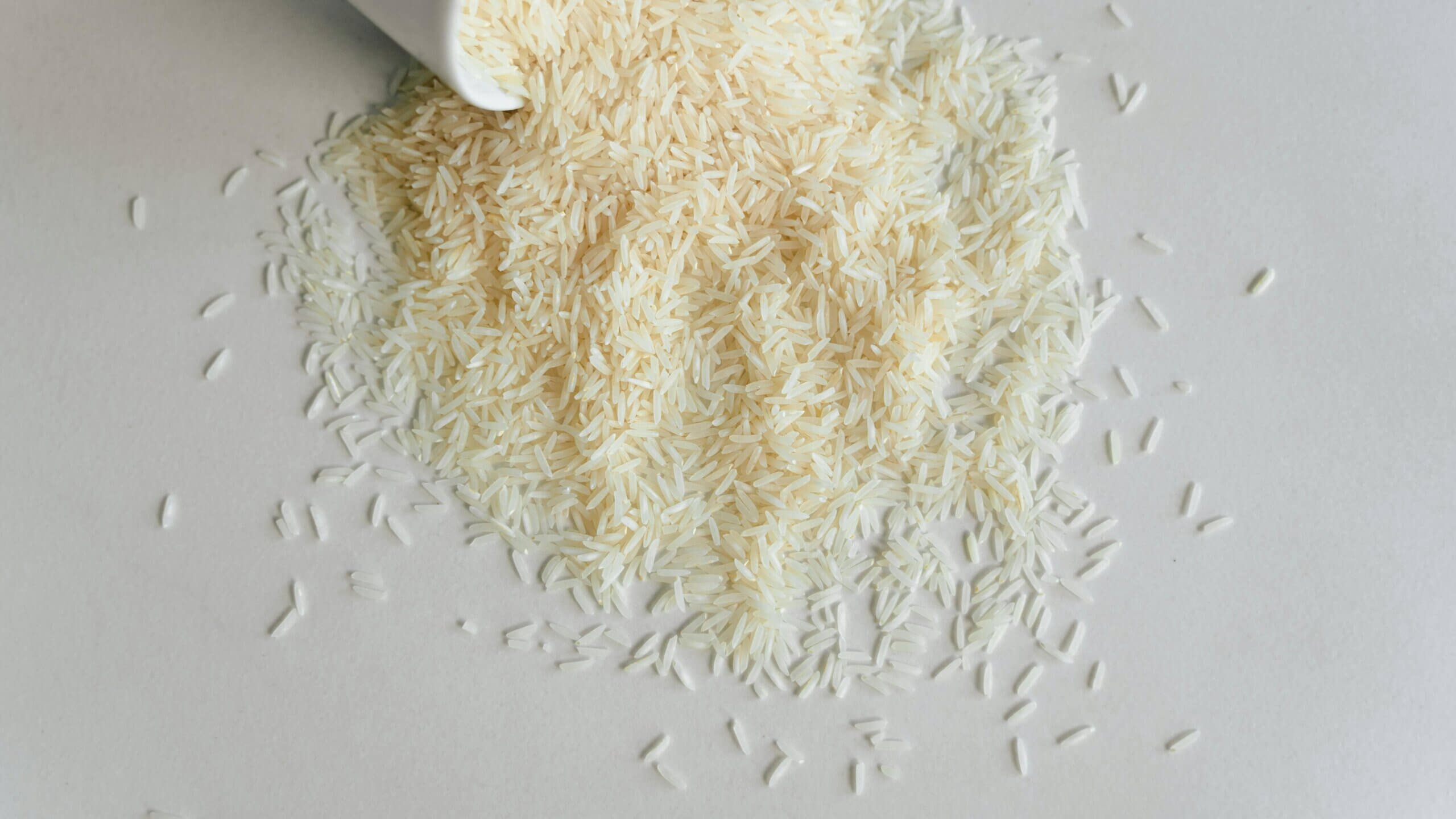 Uncooked white rice grains spilled from a white container onto a light surface.