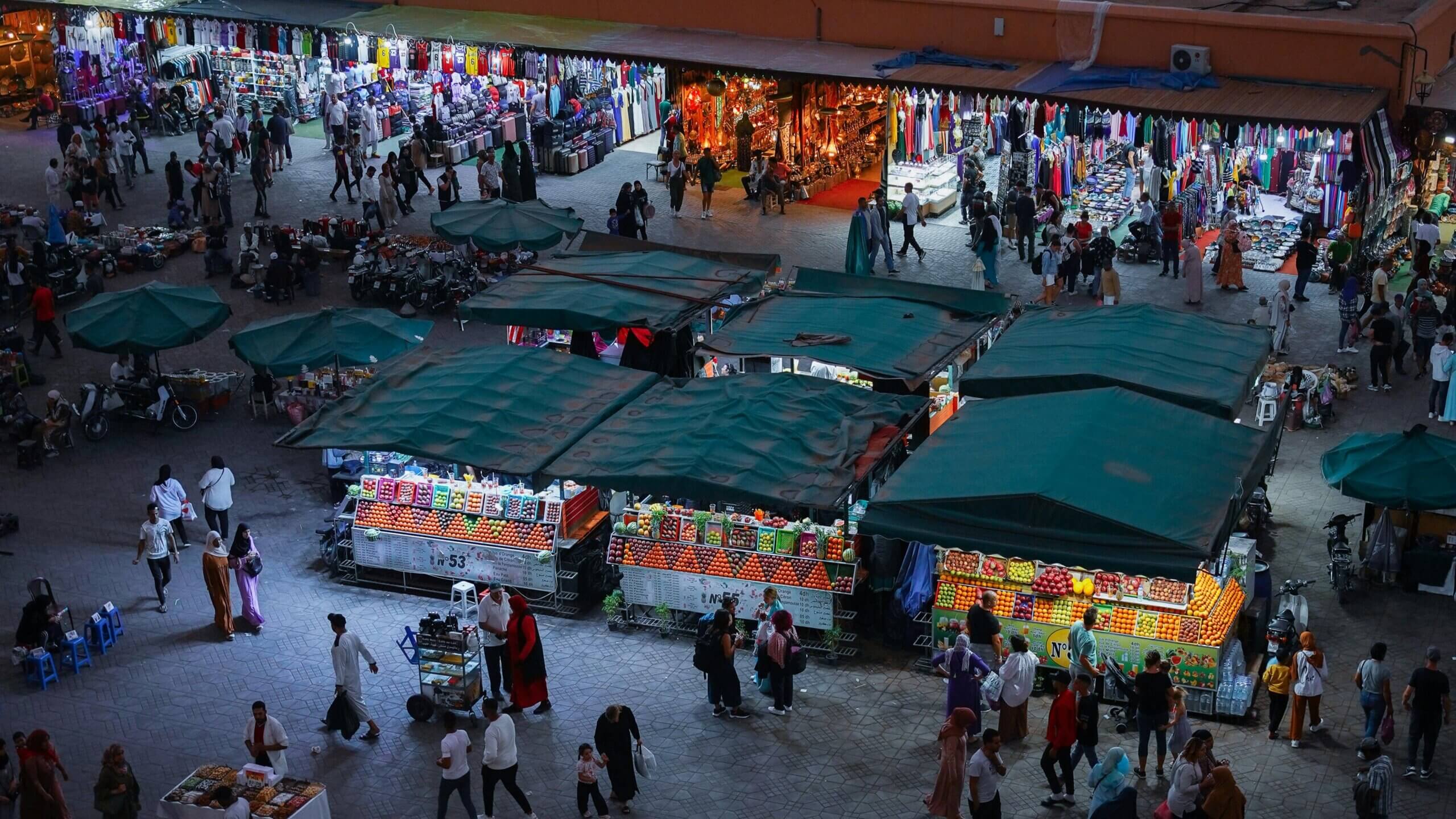 Night market with fruit stalls and clothing vendors surrounded by people shopping and walking
