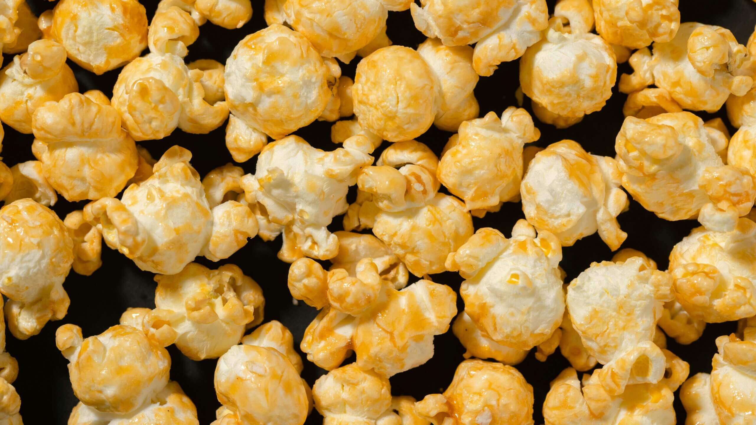 Close-up of cheddar cheese popcorn with orange seasoning on a black background