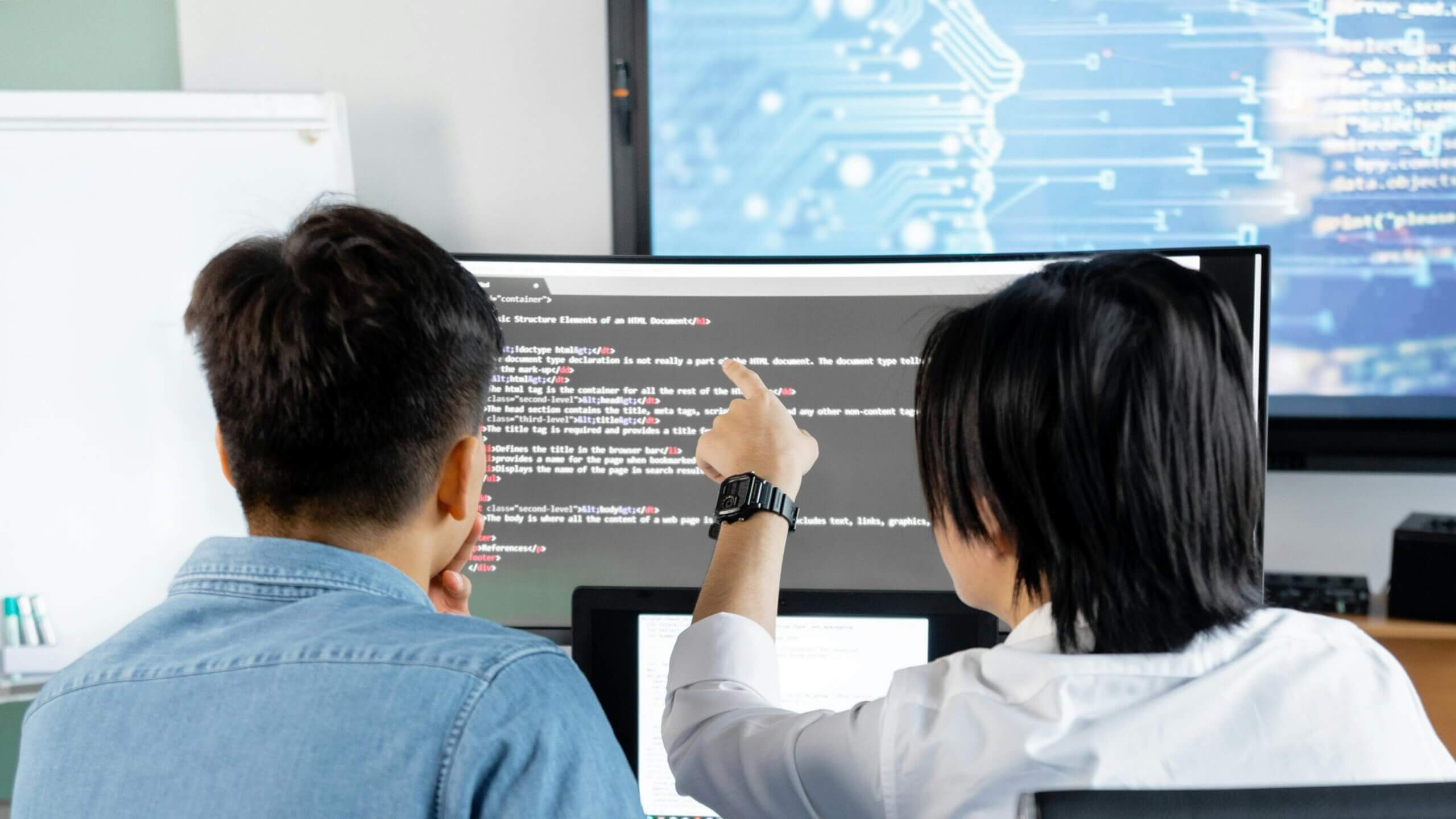 Two people reviewing HTML code on a computer screen in an office setting.