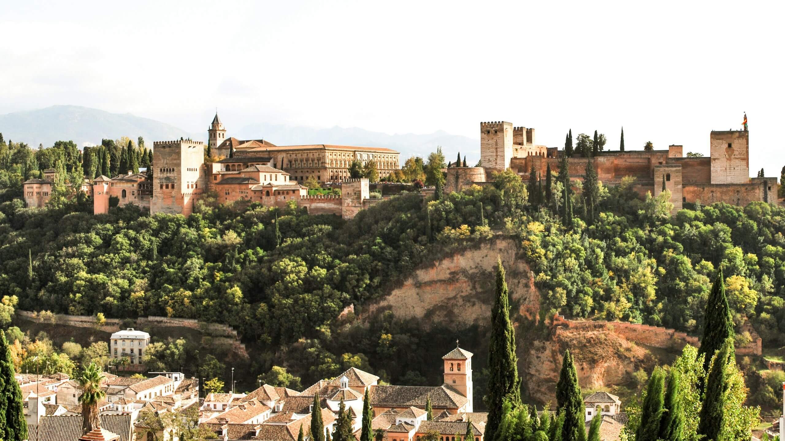 The Alhambra palace and fortress complex atop a hill surrounded by trees in Granada, Spain.