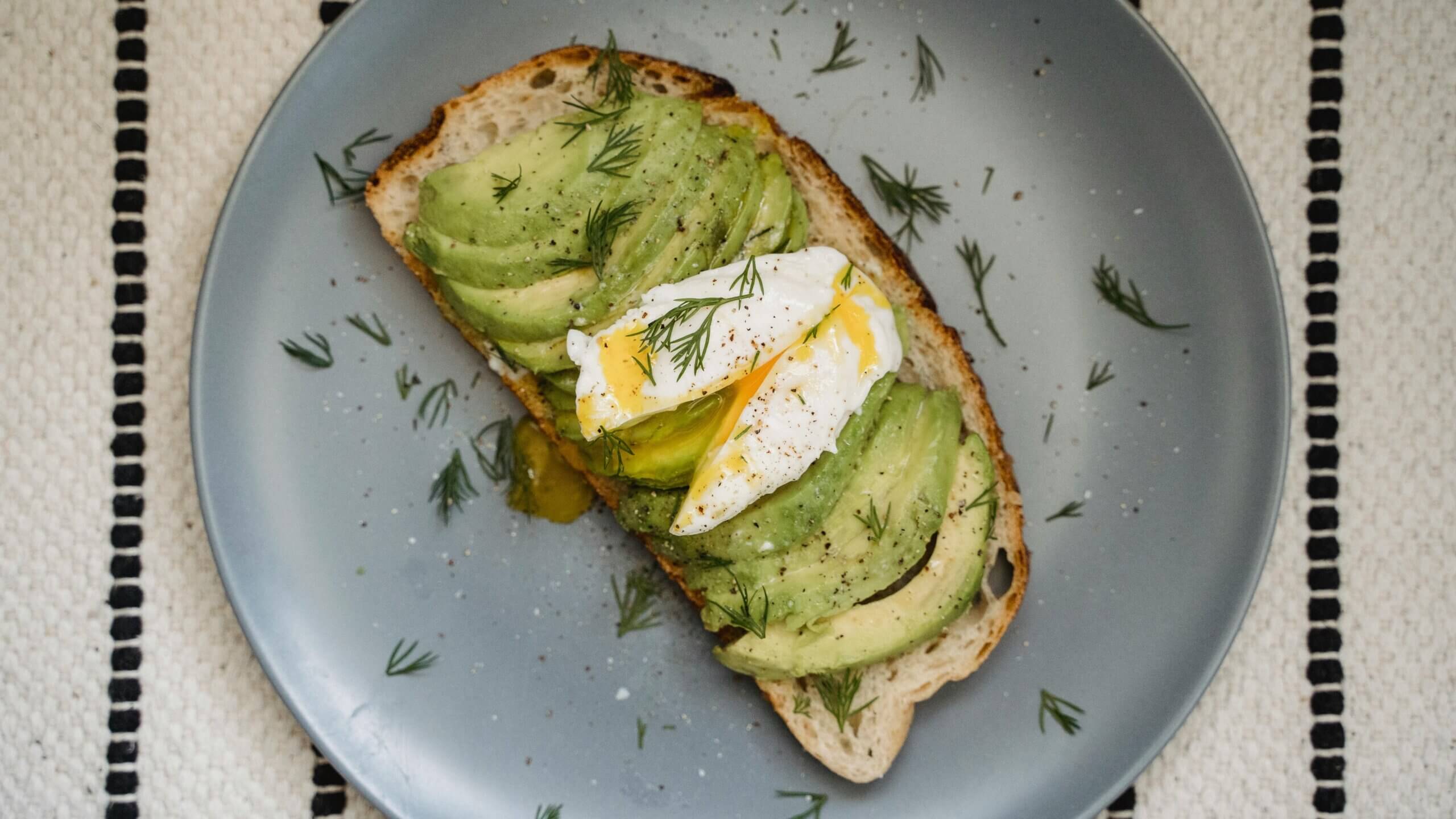 Toast topped with sliced avocado, a poached egg, and dill on a gray plate