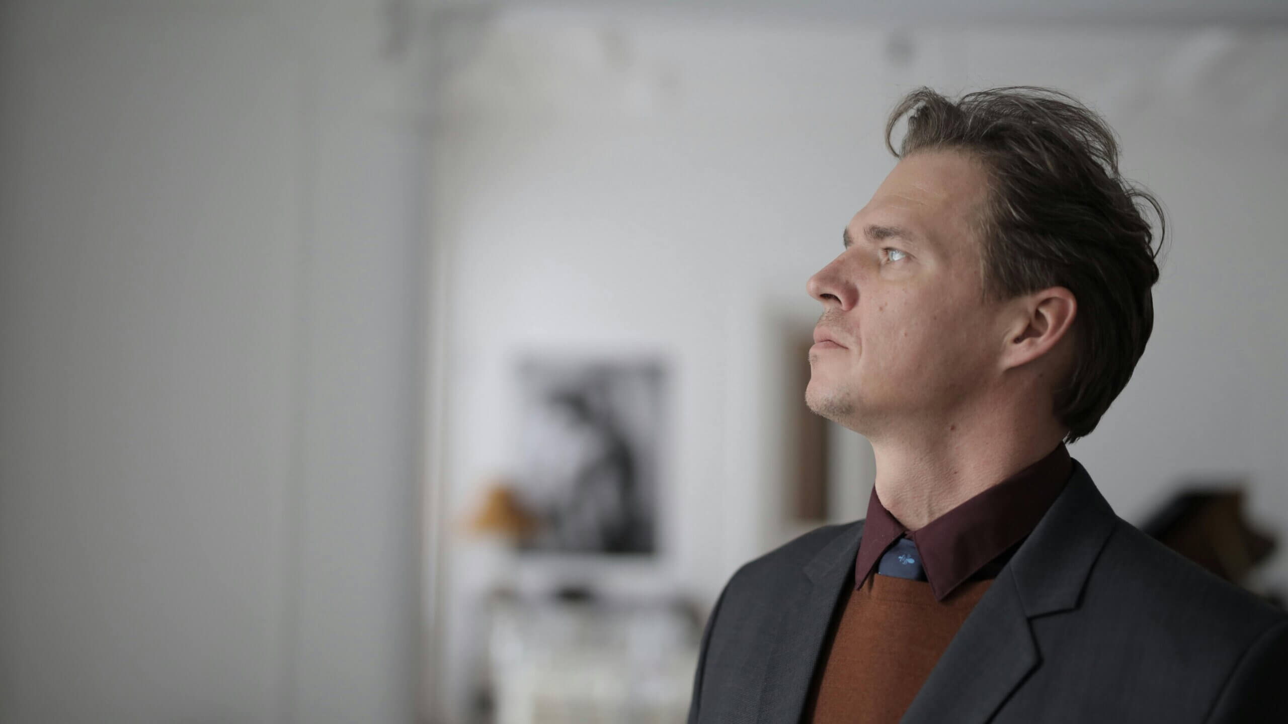 Man in suit and brown sweater looking upward in a blurred indoor setting
