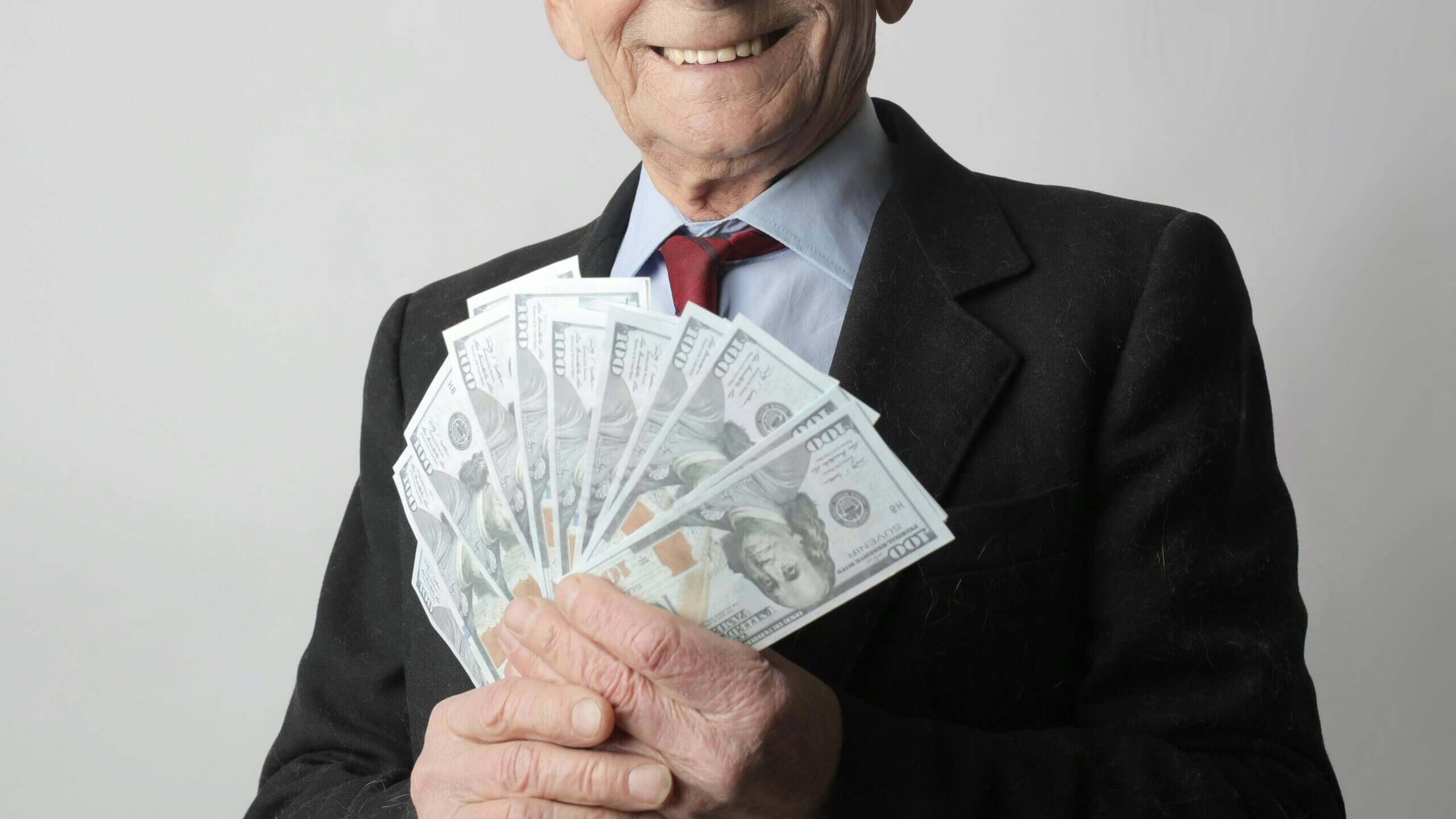 Elderly man in suit holding a fan of US $100 bills and smiling