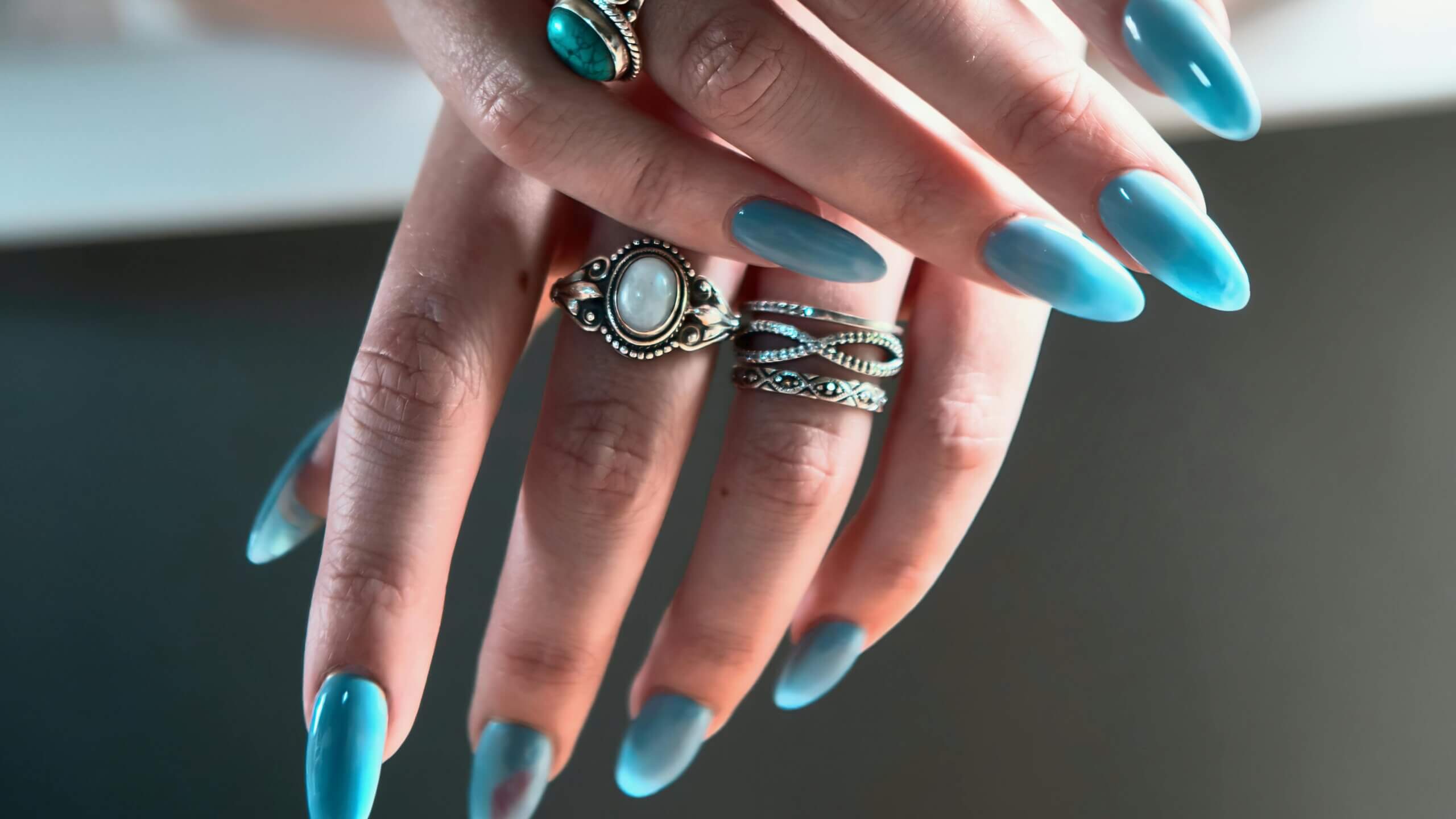 Hand with long blue nails wearing silver rings with turquoise and moonstone gemstones.