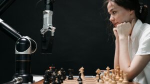 Woman in white shirt playing chess against a robotic arm on a wooden chessboard
