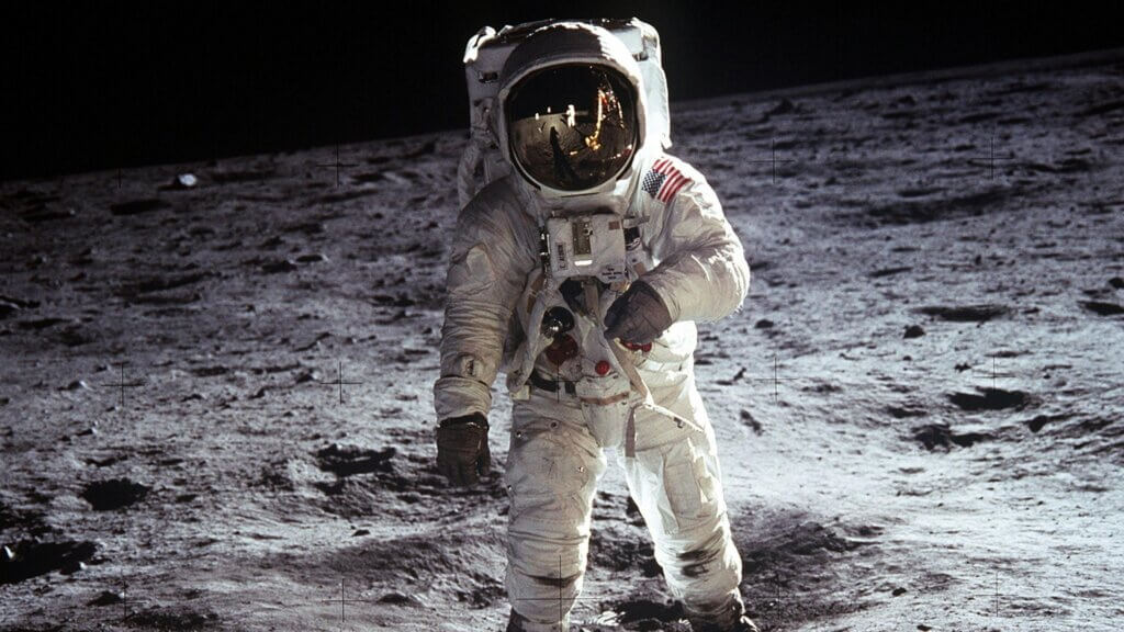 Astronaut Buzz Aldrin in a spacesuit standing on the moon with lunar surface and black sky background