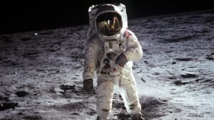 Astronaut Buzz Aldrin in a spacesuit standing on the moon with lunar surface and black sky background