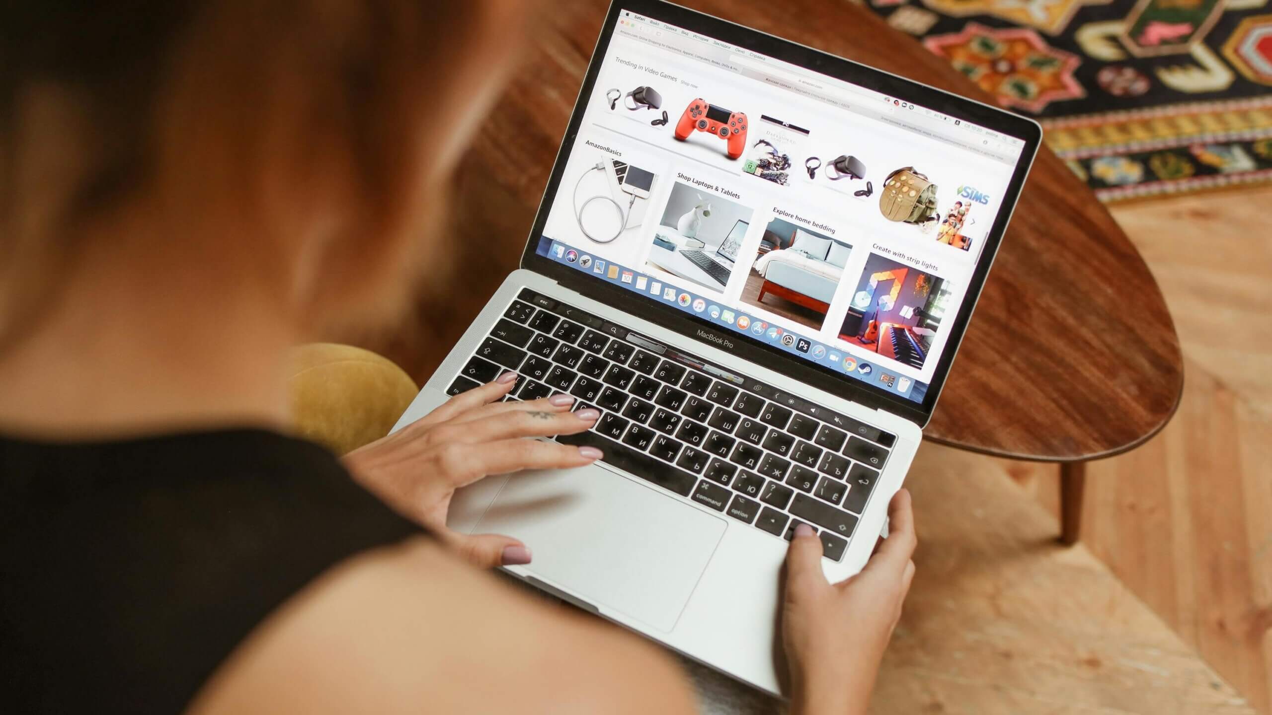 Person browsing AmazonBasics and gaming accessories on a MacBook Pro laptop at a wooden table