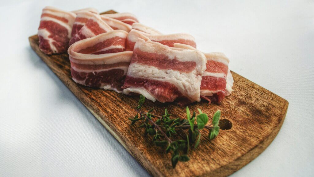 Raw pork belly slices on a wooden cutting board with fresh thyme sprigs on a white surface