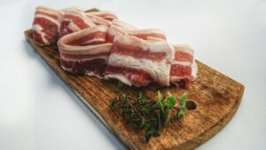 Raw pork belly slices on a wooden cutting board with fresh thyme sprigs on a white surface